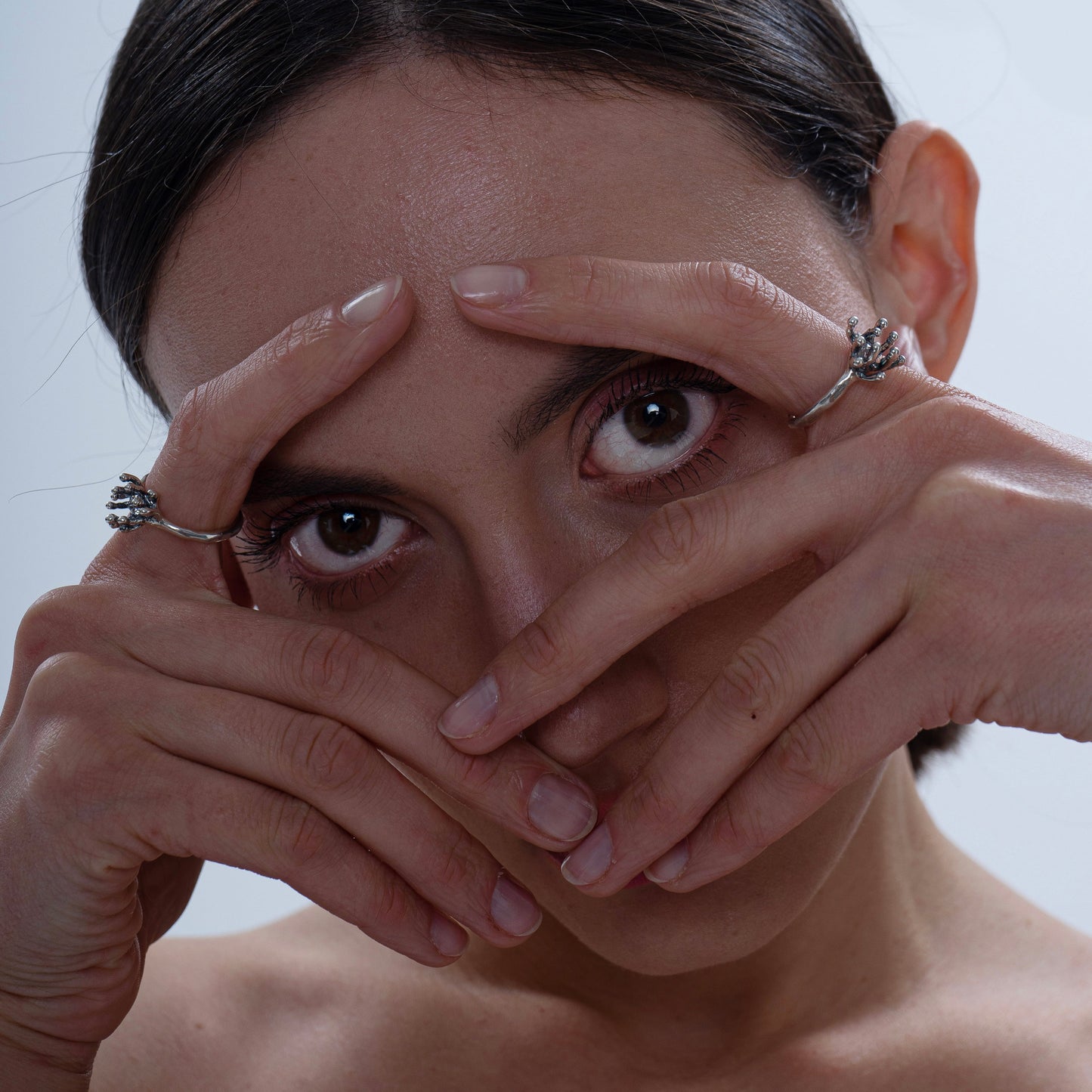 A close-up of a woman wearing the Cordyceps ring, framing her face with her hands to draw attention to the unique fungal-inspired design of the jewelry. The image captures an artistic and modern style.