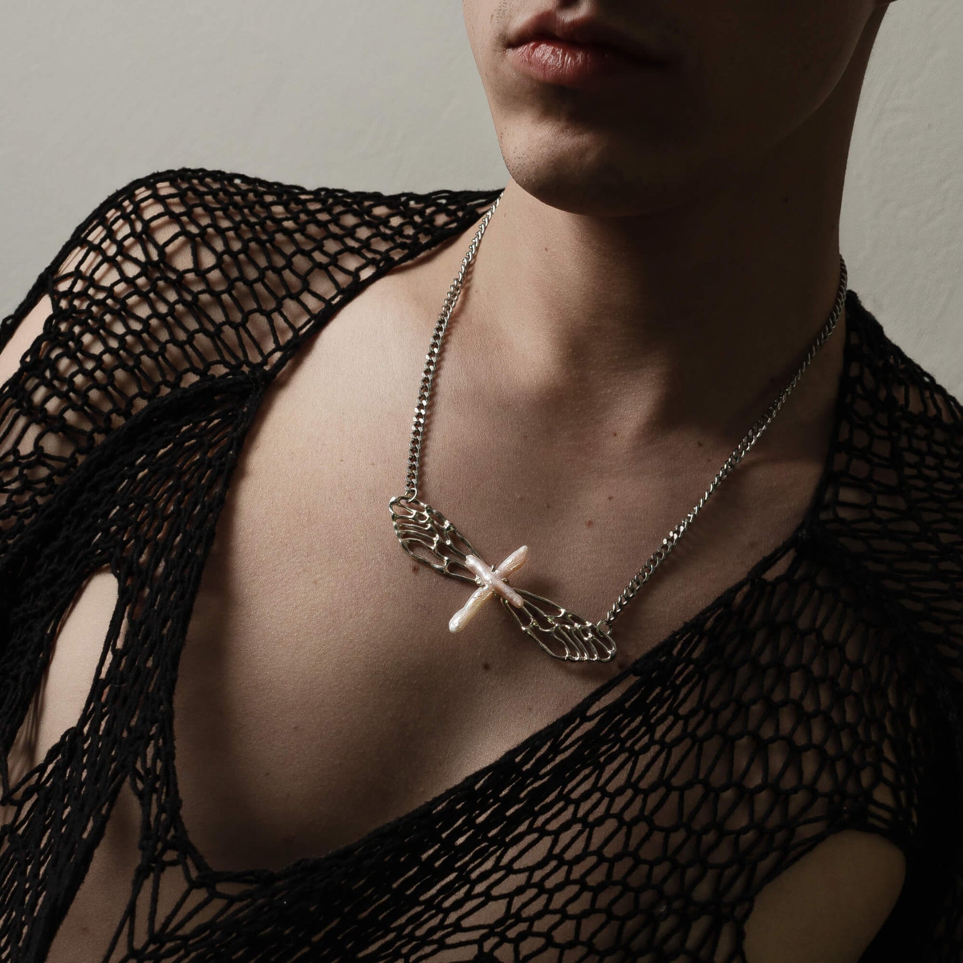 A person wearing the Metamorphosis necklace, styled with a black mesh top. The silver wings and pearl create a bold yet elegant statement, emphasizing the necklace's unique design.