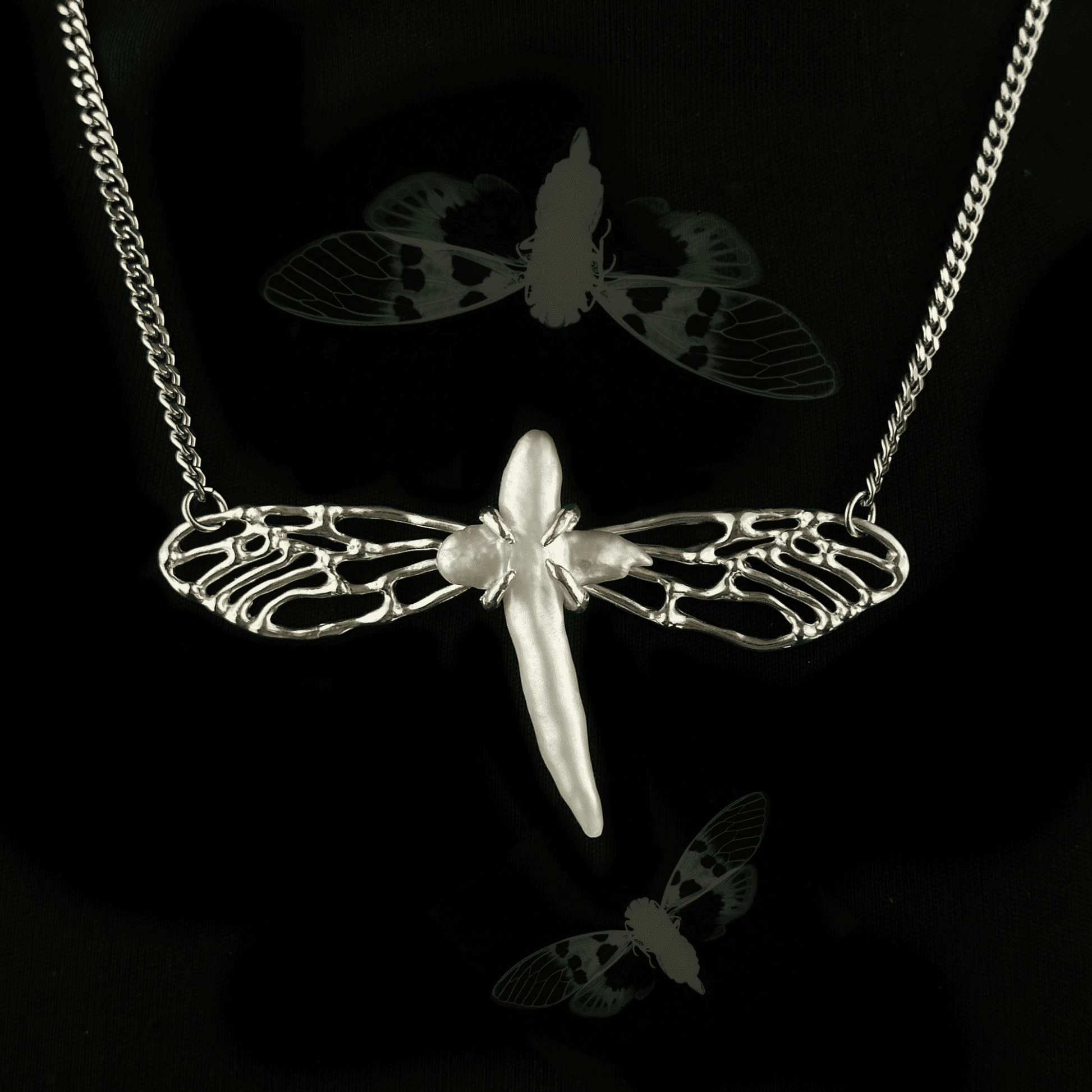 Close-up of the Metamorphosis necklace featuring a silver insect-like design with intricately crafted wings and a central pearl. The pendant symbolizes transformation, set against a dark background with faint insect imagery.