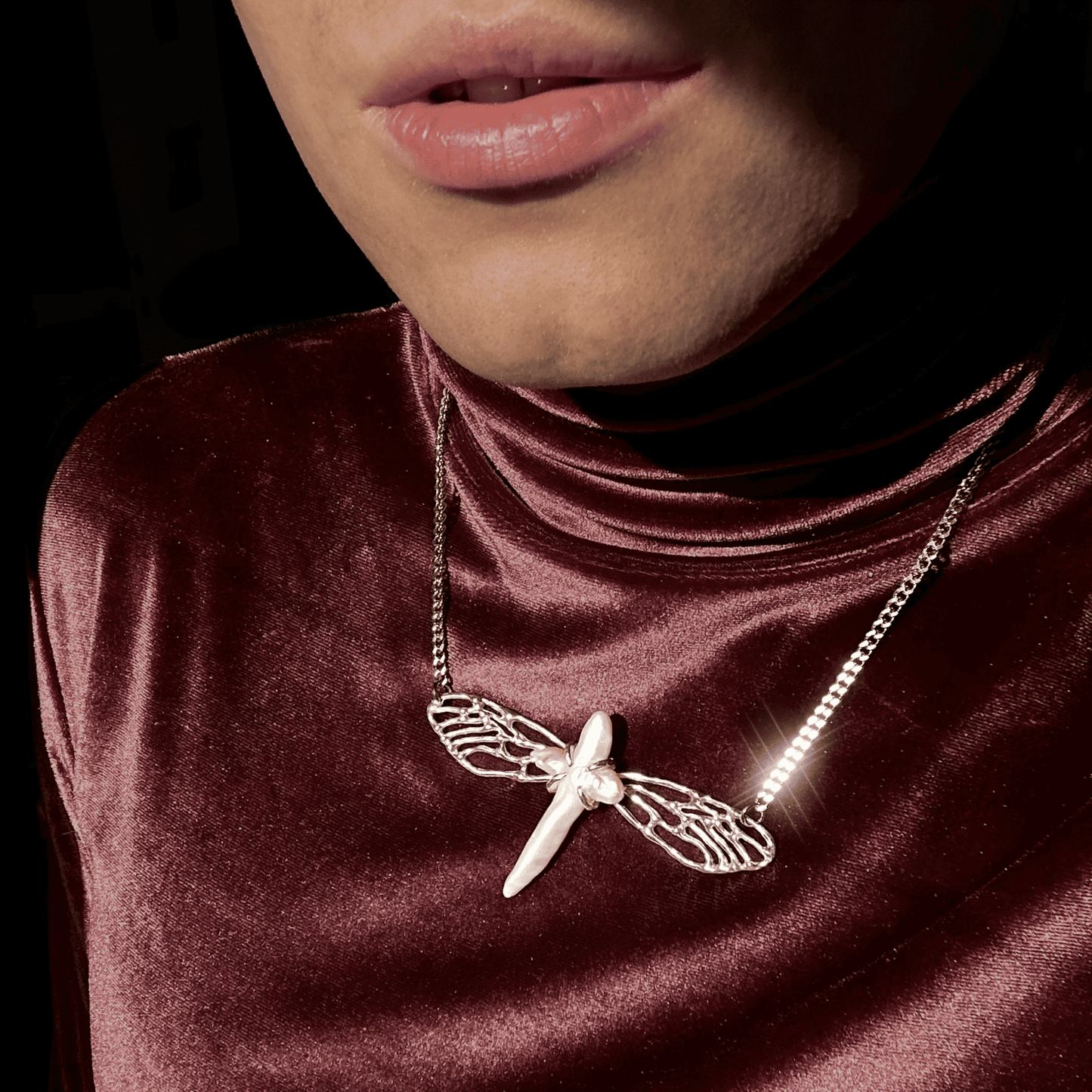 The Metamorphosis necklace worn with a red velvet high-neck top, highlighting its luxurious silver craftsmanship and the shimmering pearl centerpiece. The design stands out with a striking, artistic flair.