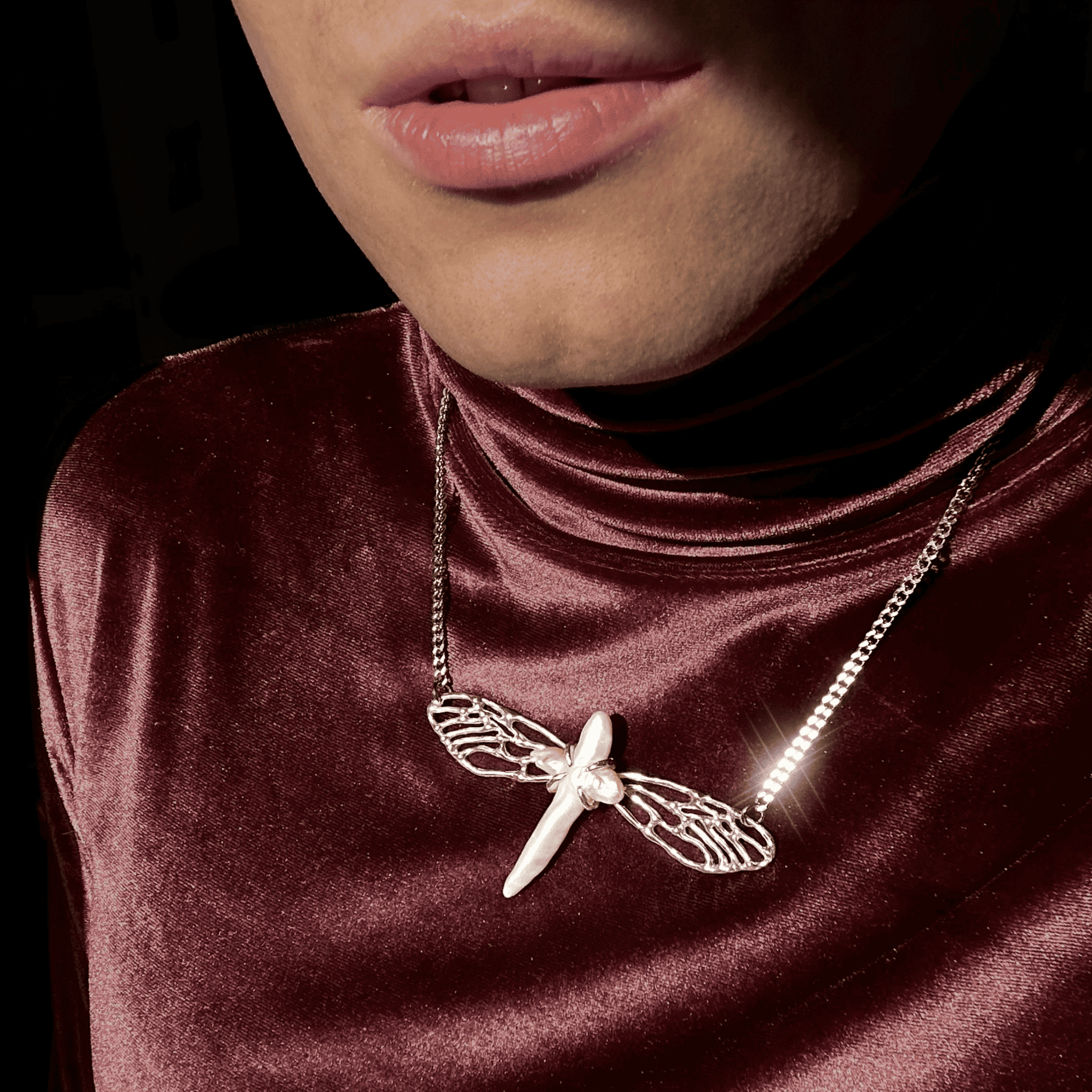 The Metamorphosis necklace worn with a red velvet high-neck top, highlighting its luxurious silver craftsmanship and the shimmering pearl centerpiece. The design stands out with a striking, artistic flair.
