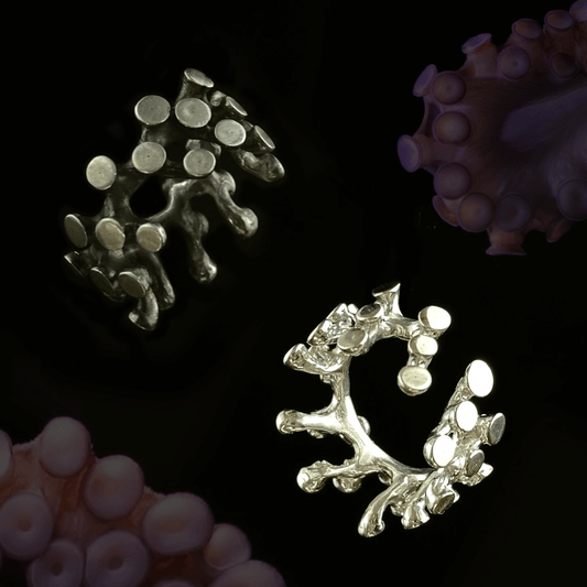 Two Octopus earcuffs displayed against a dark background, one in oxidized black and the other in polished silver. The intricate tentacle-inspired design is detailed with circular patterns, evoking the unique texture of octopus suction cups.