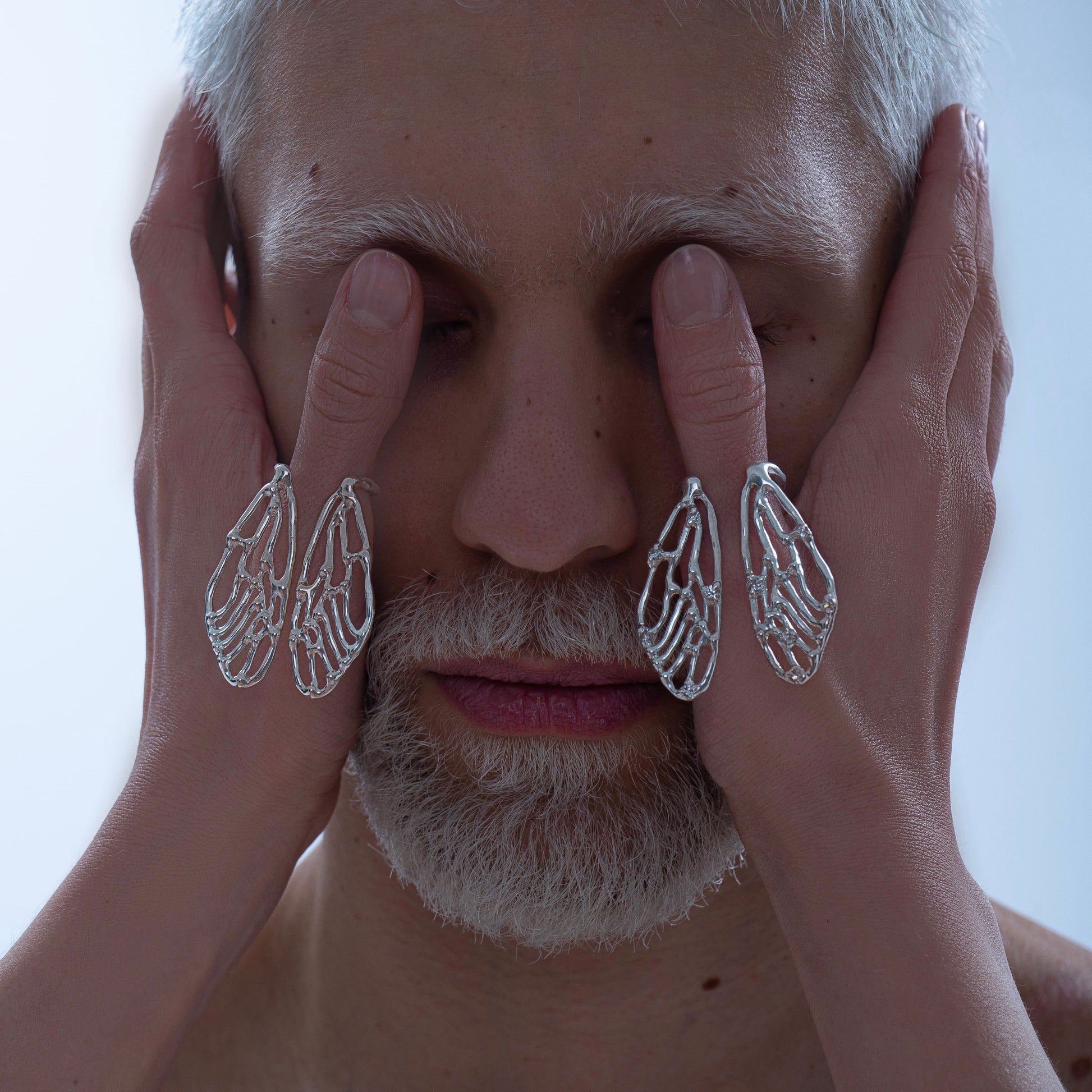 A portrait featuring the Wings Ring worn on two fingers, with the hands framing a person's face. The unique cicada wing design stands out as a statement piece in this artistic shot.